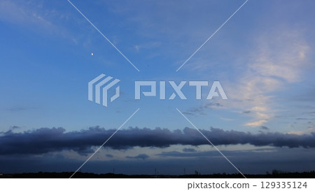 Weather: Stratocumulus clouds, roll clouds. Horizontal clouds spanning the sky under the waxing moon on a summer evening. 129335124