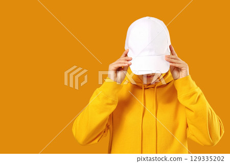 Person adjusts white cap while wearing a bright yellow hoodie 129335202