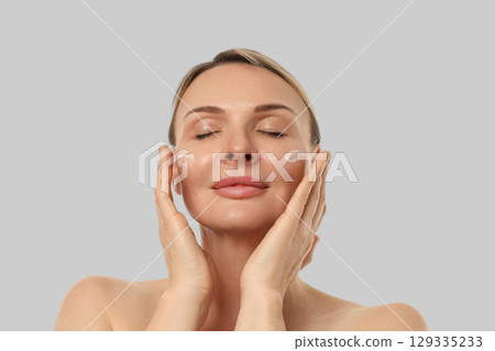 Woman gently massaging cream on her face with closed eyes Woman gently massaging cream on her face with closed eyes 129335233