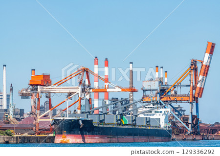 A large transport ship and gantry crane docking at the quay of the industrial complex 129336292