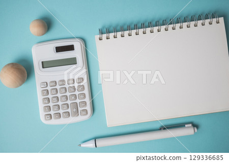 Workspace with empty notebook, calculator, pen and wooden ball on blue background. 129336685