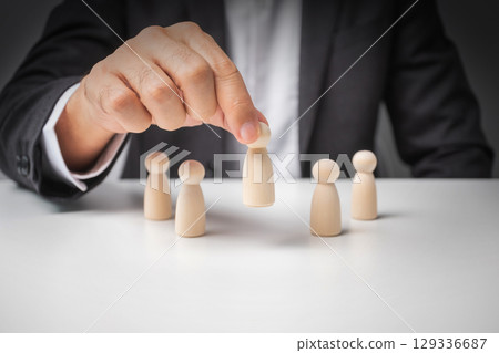 Businessman pick up leads from other wooden dolls on white desk. 129336687