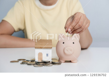Woman hand putting money coin into pink piggy bank for for savings money. 129336702