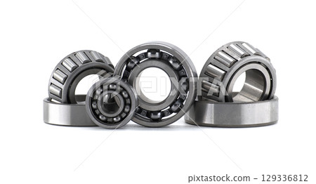 Diverse collection of mechanical ball and roller bearings sits on a clean white surface. 129336812