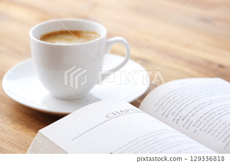 The image of someone reading a paperback while drinking coffee. 129336818