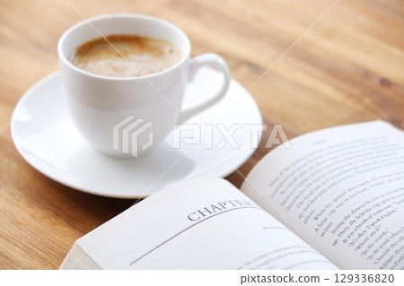 一個人一邊喝咖啡一邊悠閒地閱讀平裝書的圖像。 一個人一邊喝咖啡一邊悠閒地閱讀平裝書的圖像。 129336820