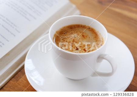 The image of someone reading a paperback while drinking coffee. 129336828