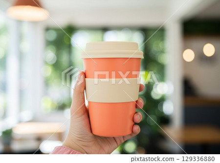 Hand holding coral and beige reusable coffee cup 129336880
