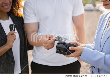 A customer is paying with a credit card at a point-of-sale terminal while a person holds a car key. A customer is paying with a credit card at a point-of-sale terminal while a person holds a car key. 129337345