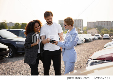 A car salesperson assists a couple with their purchase, processing a card payment at a dealership. A car salesperson assists a couple with their purchase, processing a card payment at a dealership. 129337347