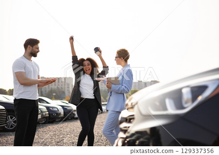 A woman celebrating a car purchase, holding keys, next to a car, with a salesperson and another man. 129337356
