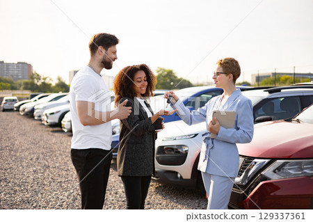 A car salesperson hands over keys to a couple at a car dealership, symbolizing a successful purchase. 129337361