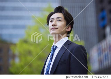 一位身著西裝的日本商人凝視遠方，背景則是一棟建築 129337834