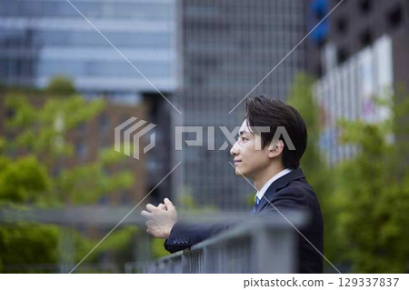A Japanese businessman in a suit gazing into the distance with a building in the background A Japanese businessman in a suit gazing into the distance with a building in the background 129337837