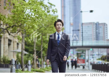一位身著西裝的日本年輕男子在商業區行走 129337858
