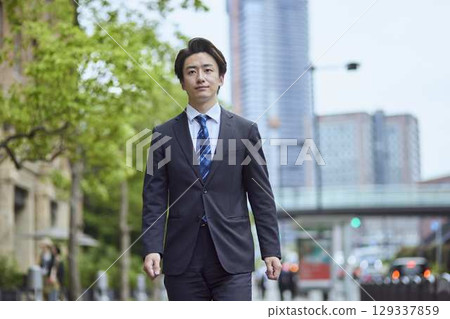 一位身著西裝的日本年輕男子在商業區行走 129337859