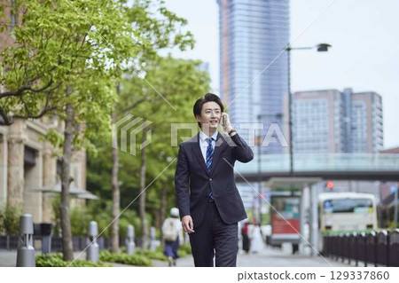 一位年輕的日本商人一邊走路一邊用智慧型手機說話 129337860