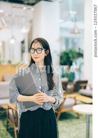 Businesswoman carrying a laptop in the office 129337867