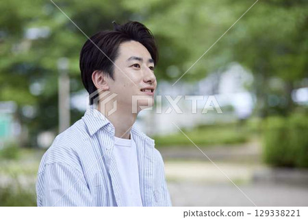 A smiling young Japanese man relaxing in a park on his day off 129338221