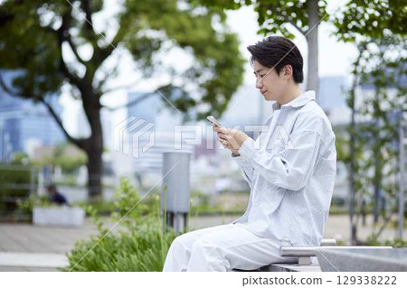 A Japanese man in casual clothes relaxing in a park on a holiday and using his smartphone 129338222