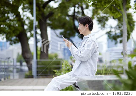 A Japanese man in casual clothes relaxing in a park on a holiday and using his smartphone 129338223