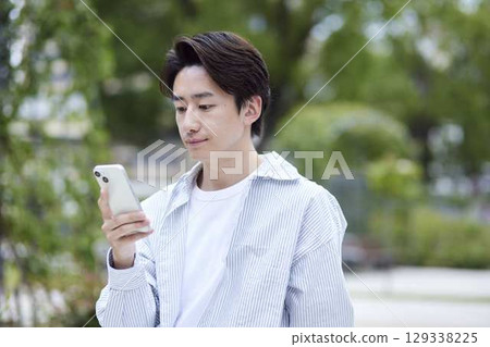 一位身著休閒服的日本男子在假期期間在公園休息並使用智慧型手機 129338225