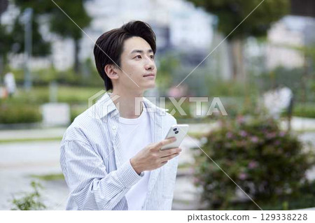 A young Japanese man holding a smartphone in a park A young Japanese man holding a smartphone in a park 129338228