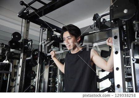 A young man prepares to do squats, with a barbell on his shoulders. A young man prepares to do squats, with a barbell on his shoulders. 129338258