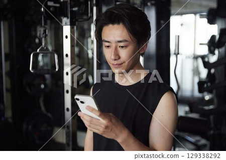 Japanese man checking information on his smartphone at a gym. Japanese man checking information on his smartphone at a gym. 129338292