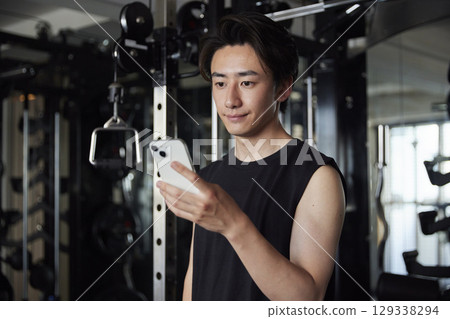 A man enters his training records on his smartphone at the gym. A man enters his training records on his smartphone at the gym. 129338294