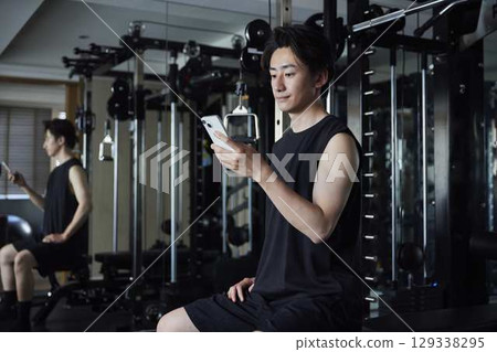 A healthy young Japanese man operating a smartphone at a fitness gym 129338295
