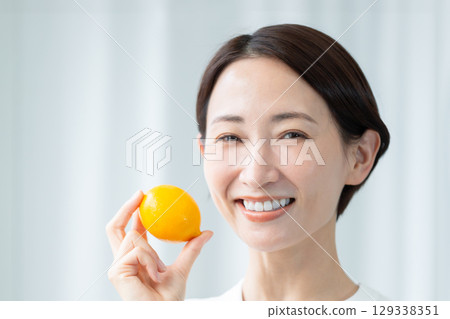 一位面容清秀的女士手捧檸檬，露出清新的笑容。特寫照片。 129338351