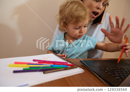 Mother Balancing Remote Work While Engaging with Curious Toddler at Home 129338569