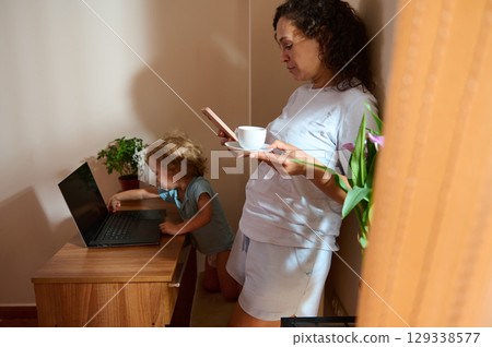 Mother Working from Home Balancing Freelance Tasks and Childcare in Cozy Ambiance 129338577