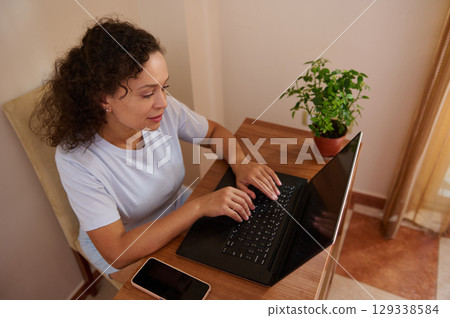 Focused Woman Typing on Laptop While Working in a Cozy Home Environment Focused Woman Typing on Laptop While Working in a Cozy Home Environment 129338584