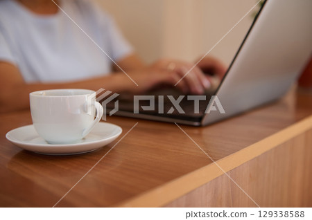 Young Woman Working Remotely on Laptop While Enjoying a Cup of Coffee in Cozy Home Interior Young Woman Working Remotely on Laptop While Enjoying a Cup of Coffee in Cozy Home Interior 129338588