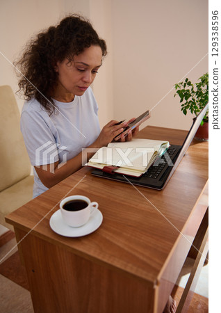 Woman Working from Home Using a Laptop, Phone, and Planner Woman Working from Home Using a Laptop, Phone, and Planner 129338596