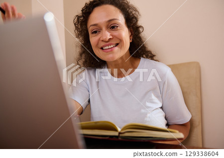 Smiling Woman Working Remotely from Home With a Notebook and Laptop 129338604