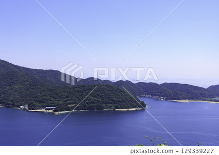 The view of Moon Beach from the Sada Misaki Peninsula. A beautiful landscape of blue ocean, lush green mountains, and golden sand beaches. 129339227