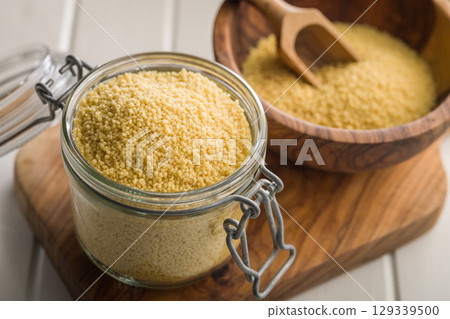 Raw couscous in jar on wooden cutting board. 129339500