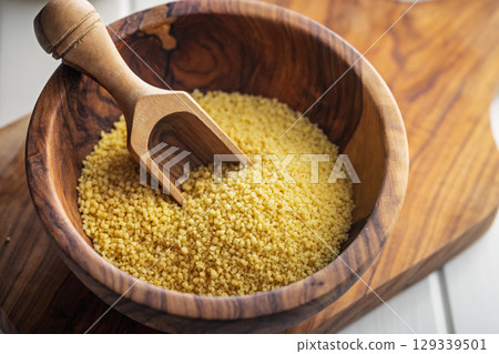 Raw couscous in bowl on wooden cutting board. Raw couscous in bowl on wooden cutting board. 129339501