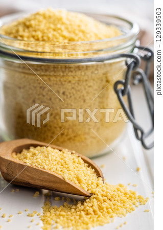 Raw couscous in wooden scoop on white table. 129339503