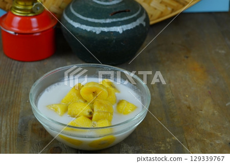 A glass bowl of kolak pisang or Indonesian banana compote in coconut milk, with a red oil lamp and a traditional clay pot in the background. A glass bowl of kolak pisang or Indonesian banana compote in coconut milk, with a red oil lamp and a traditional clay pot in the background. 129339767