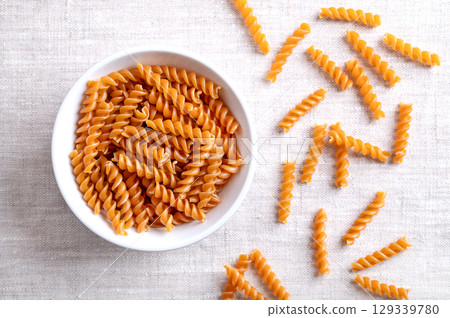 Chickpea spiral pasta, gluten free noodles in a white bowl on linen fabric. Small fusilli, a pasta variety, with helical or corkscrew shape, made of chickpea flour, an alternative to wheat flour. 129339780