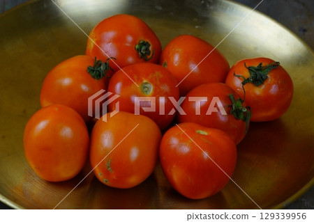 A pile of fresh, ripe tomatoes on a golden brass plate. 129339956