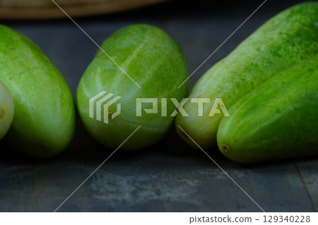 A horizontal line of fresh, green cucumbers laid out on a rustic wooden surface. 129340228