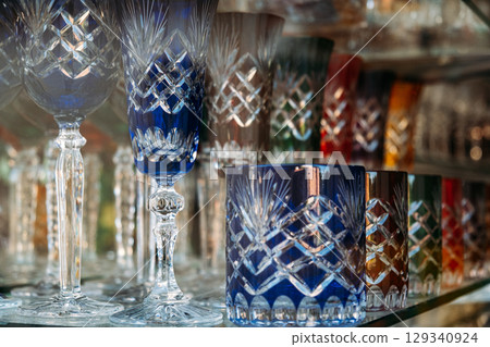 Colorful cut crystal glassware arranged on a shelf in a store display. Craftsmanship, artisanal glassmaking, decorative objects, luxury homeware 129340924