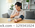 An Asian woman uses a portable blood pressure monitor in her living room. Health awareness concept. 129341024
