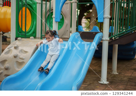 happy toddler baby girl sliding and playing at playground 129341244