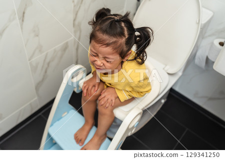 toddler girl sitting on toilet at home and suffering from stomachache and constipation 129341250
